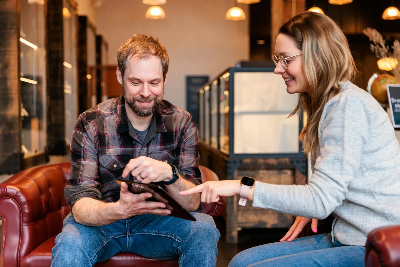 Inhaber eines Handwerksbetriebs zeigt einer Kundin die JungMedien-App auf dem Tablet in der Werkstatt.